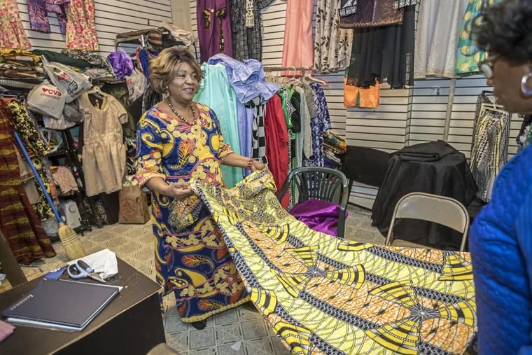 Ngozi Oguekwe, left, the owner of Ngozi African Fashions, stretches out one of the dresses she has sewn for a customers.