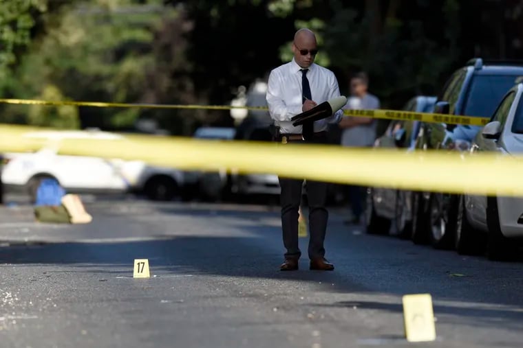 A Philadelphia Police investigator examines the scene of a triple shooting in Graduate Hospital in August.