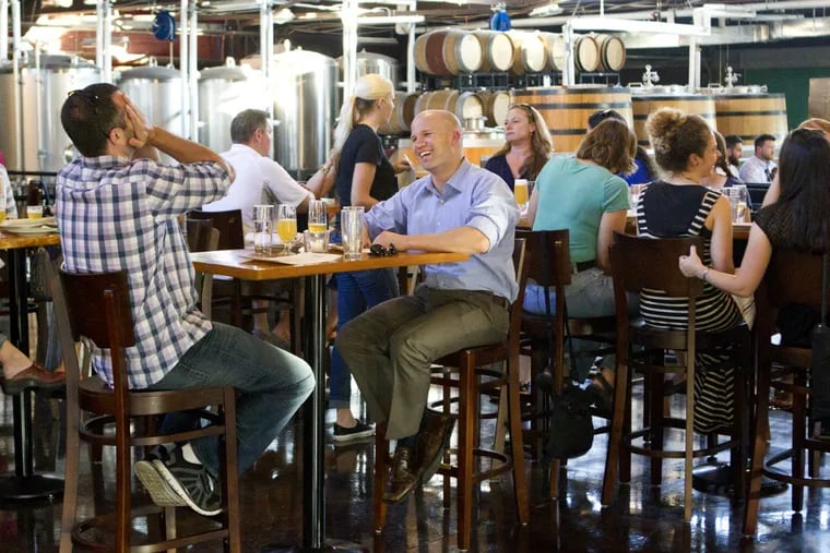 Diners at Tired Hands Fermentaria in Ardmore, surrounded by barrels and brewing equipment.