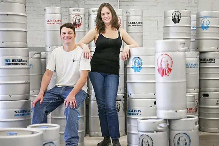 Tim Patton and Christina Burris gather around some kegs at their new St. Benjamin Brewing Co. on 5th Street near Cecil B. Moore Avenue in North Philadelphia. The three-barrel nanobrewry is opening up just in time for Philly Beer Week. (David Maialetti/Staff)