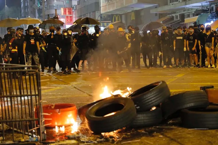 Black-clad protestors stand near burning tires in Hong Kong, Tuesday, Oct. 1, 2019.