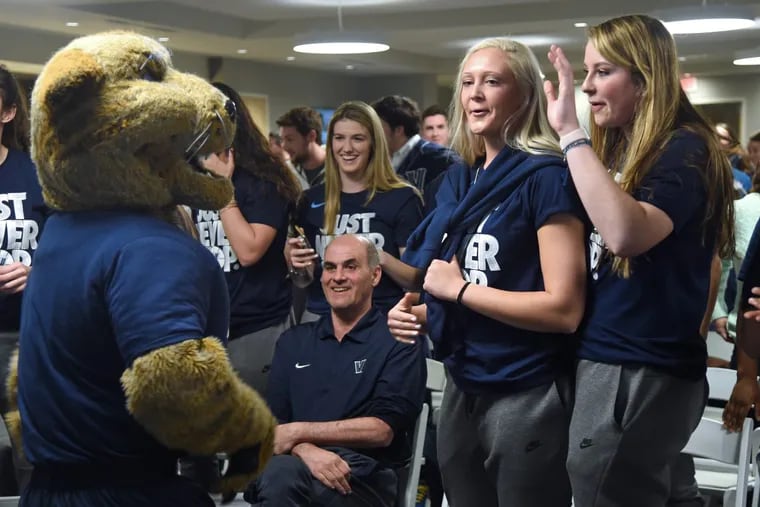 Villanova women’s coach Harry Perretta remains seated as players Megan Quinn (right) and Alex Louin (left) react with the Wildcats' mascots at the announcement of their seed during an NCAA selection viewing on campus.