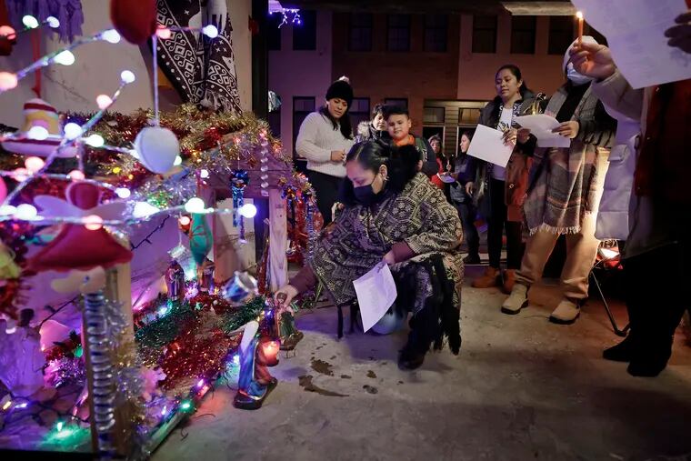 Mayra Rufino (kneeling) presents statues of Joseph and Mary as members of the Mercado de Latinas (women of Reyna Guadalupe Navarro Mexican and Central American heritage who sell arts and crafts in South Philly's Capitolo Playground) sing Christmas carols during a posada at Reyna Guadalupe Navarro’s home in South Philadelphia on Dec. 17, 2021.