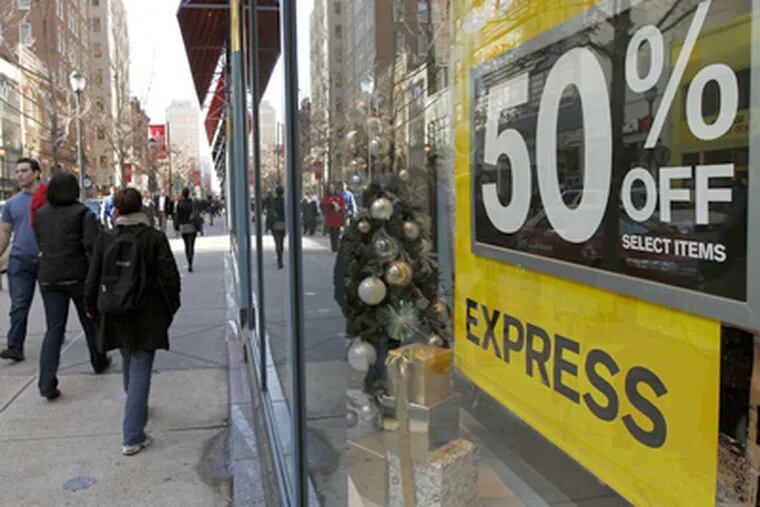 Pedestrians walk a shopping district as Express advertises a sale during the unseasonably warm weather in the few days before Christmas Thursday, Dec. 22, in Philadelphia. (AP Photo/Alex Brandon)