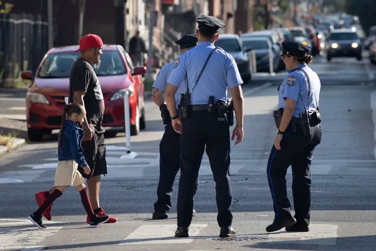 Philadelphia police as a parent and student cross Jasper Street after an overnight shooting near Frances E. Willard Elementary School.