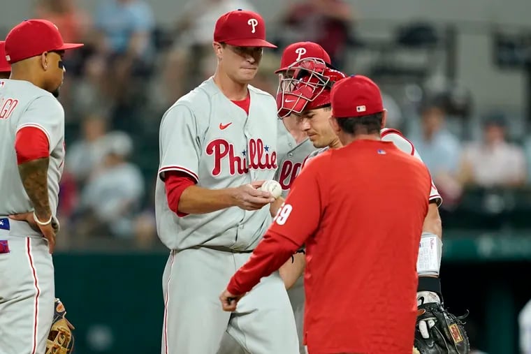 Philadelphia Phillies' Johan Camargo, left, and catcher J.T. Realmuto stand on the mound as starting pitcher Kyle Gibson turns the ball over to interim manager Rob Thomson, front, in the seventh inning of a baseball game against the Texas Rangers, Tuesday, June 21, 2022, in Arlington, Texas. (AP Photo/Tony Gutierrez)