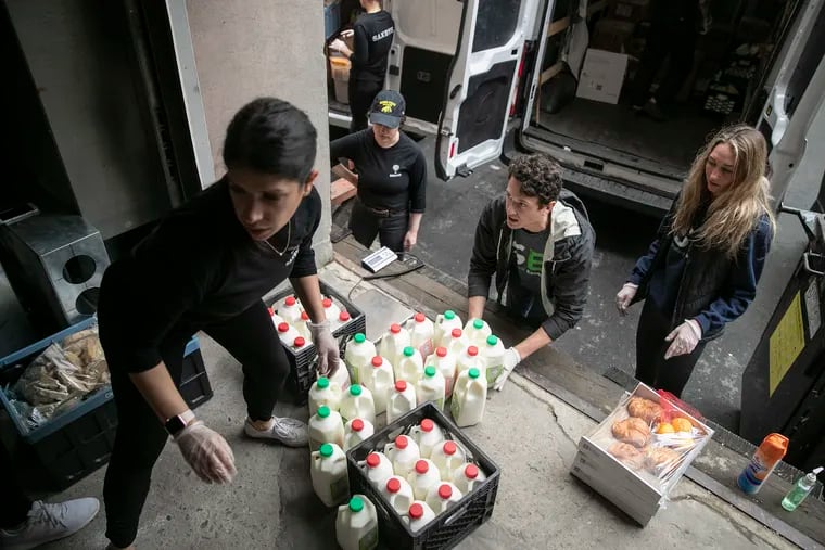 Evan Ehlers (right), founder of Sharing Excess, a Philadelphia-based nonprofit that helps connect grocery stores and restaurants with surplus food to hunger-relief organizations with storage space, lifts up milk to weigh and load in a truck from Saxby's employee Haley Samsi (left).