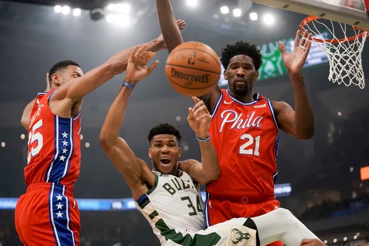 Milwaukee Bucks' Giannis Antetokounmpo is fouled as he drives between Philadelphia 76ers' Ben Simmons and Joel Embiid (21) during the first quarter on Saturday night's game. Simmons exited the game in the first quarter.
