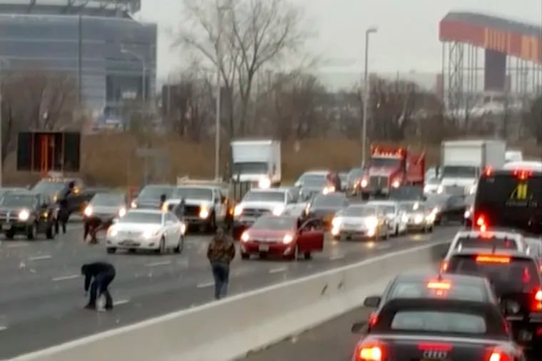 This screen shot from a video provided by Danielle Shah shows people picking up cash that spilled from an armored truck onto the highway in East Rutherford, N.J., near MetLife Stadium, Thursday, Dec. 13, 2018. Police say the incident caused multiple crashes as motorists stopped to grab the money from the truck that authorities say apparently had an issue with the locking device on one of its doors. (Danielle Shah/@dbholden417 via AP)