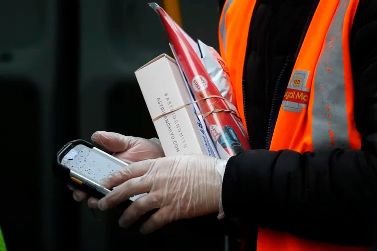 A Royal Mail employee wears gloves as he hold parcels and the signature handheld as he delivers in London.