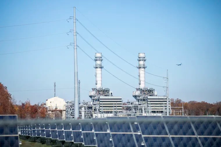 The West Deptford Energy LLC power station, fueled by natural gas, is viewed behind a field of solar panels in Paulsboro, N.J. Rising energy prices on the regional power grid have caused customer rates to increase at many Pennsylvania electric utilities.
