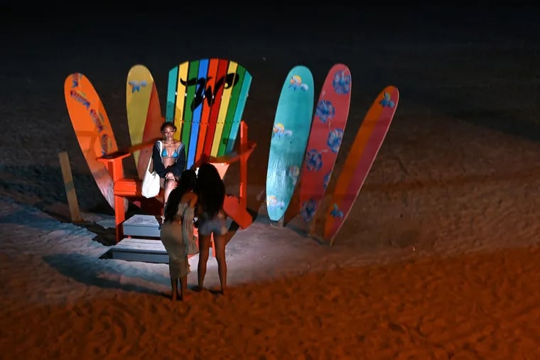 May 30, 2022: Nighttime beach-goers take flash photos on the big chair and surfboards, in the dark, just off the boardwalk in Wildwood.