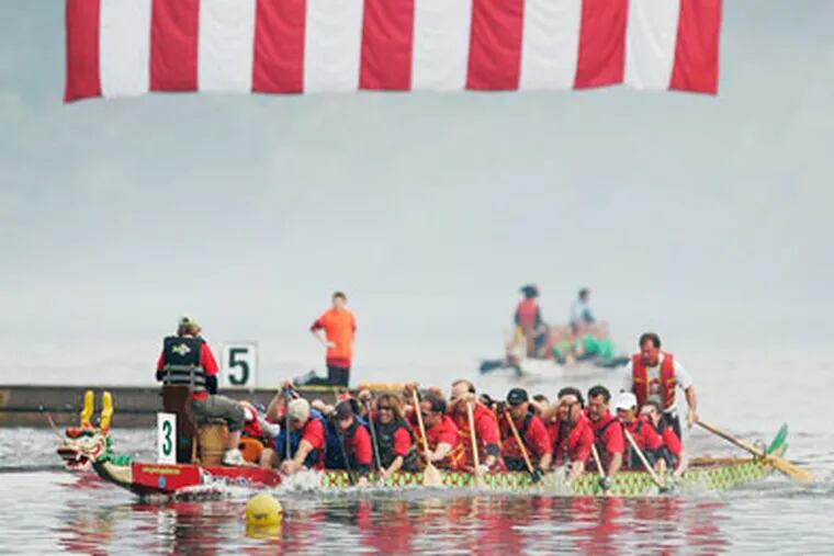 Dragon boat #3 Wyeth Wyverns paddle down the Schuylkill river in the 10th race of the morning. The huge American flag that was hanging fromthe Strawberry Mansion Bridge was reflected in the river. ( Michael Bryant / Staff Photographer )