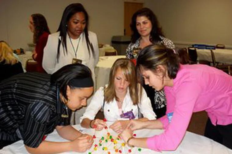 Burlington Twp. High students Jozsalina Delval, Michelle Hickey and Kelly Pawlak build a support tower made of gum drops and toothpicks, part of the County Advisory Council on Women&#0039;s Reach for the Stars mentoring program at Lockheed Martin in Moorestown. Lockheed volunteer Arlene Brooks and Freeholder Dawn Marie Addiego watch.