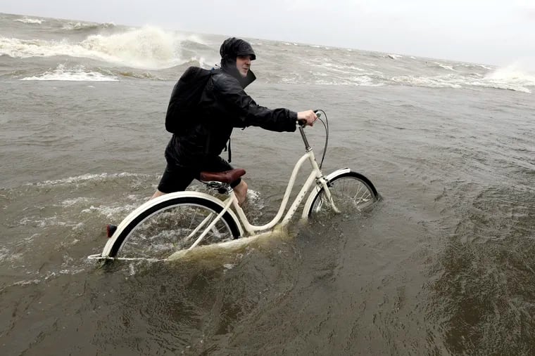 Tyler Holland guides his bike through the water as winds from Tropical Storm Barry push water from Lake Pontchartrain over the seawall Saturday, July 13, 2019, in Mandeville, La. (AP Photo/David J. Phillip)