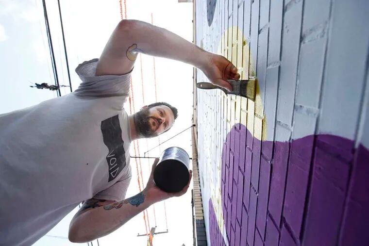 Ryan Beck paints a mural at 1016 Buttonwood St. in the city’s Callowhill section, part of developer Craig Grossman’s plan to rebrand the area between Ninth and 12th Streets from Noble to Spring Garden. 
MICHAEL BRYANT / Philadelphia Inquirer