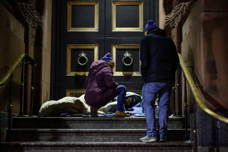 An unhoused person sleeps on the steps of the Basilica of SS. Peter and Paul on 18th Street as Amy Herlich (left) and Tom Marvit conduct the city's winter count of people living on the streets in January.
