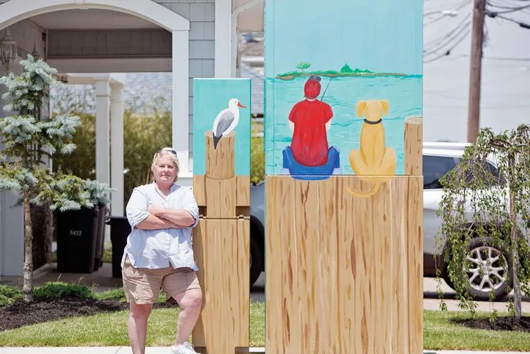 Carla Migliaccio with her painting of a boy fishing with his dog in Ocean City. It is at 10th Street and Bay Avenue. (ED HILLE/Staff Photographer)