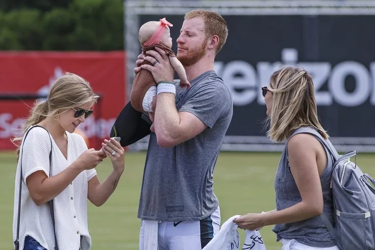 Philadelphia Eagle Carson Wentz, center, goes eye to eye with an infant after practice at the Eagles training camp, as his wife, Madison Oberg, left, checks out the photo she took of the two of them, at the NovaCare Center on August 2, 2018. MICHAEL BRYANT / Staff Photographer