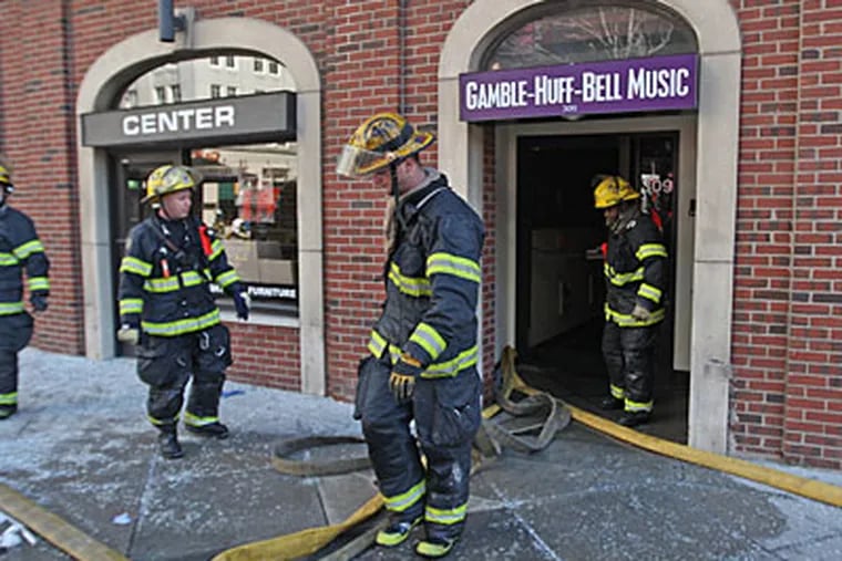 Firefighters drag equipment out of the front door of 309 South Broad Street, home of Philadelphia International Records, after a fire engulfed the top floors of the building. ( Michael Bryant / Staff Photographer )