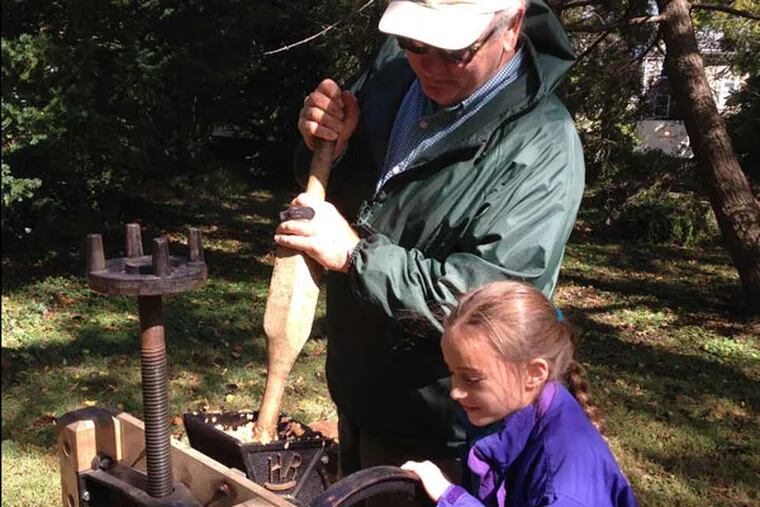 Scott Blunk, a retired farmer who now volunteers at Weavers Way, shows Gretta Maguire, 8, how to make all-natural apple juice in an old-fashioned press. "Why don't we volunteer?" Gretta asked her father. Photo Julie Zauzmer