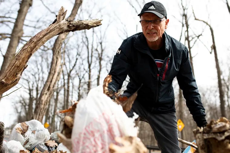 Madis Pihlak, 66, of Bluebell Hill, Philadelphia, retired professor from Penn State University, uncovers a pile of grocery bags filled with trash underneath leaves alongside Walnut Lane. He has been picking up trash near his home since January.