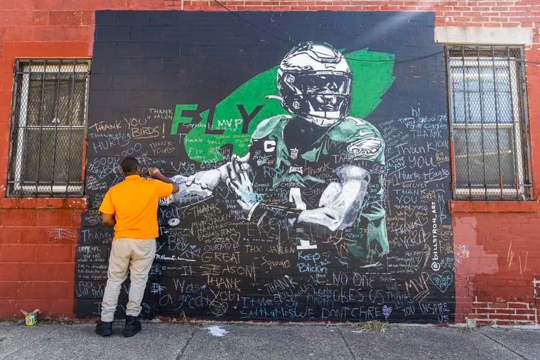 Charles Allen, 26, of North Philadelphia, writes a “thank you” message on the Jalen Hurts mural in Philadelphia.