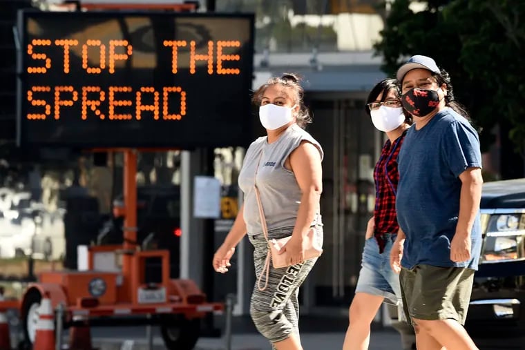 FILE - Pedestrians wear masks as they walk in front of a sign reminding the public to take steps to stop the spread of coronavirus, Thursday, July 23, 2020, in Glendale, Calif. Los Angeles County is seeing some hopeful signs amid the coronavirus surge. The county reported Wednesday that COVID-19 hospitalization and transmission rates are dropping. (AP Photo/Chris Pizzello, File)