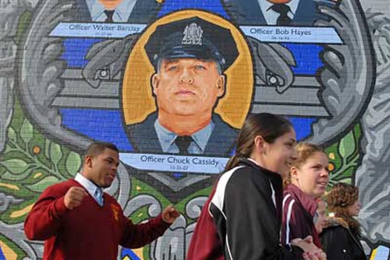 Students from Cardinal Dougherty High School pass by a mural at the 35th Police District which honors police killed in the line of duty. The students gave baked goods to officers of the 35th on Wednesday.  (Peter Tobia / Staff Photographer)