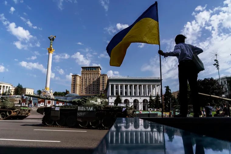 A woman holds the flag of Ukraine while looking over a row of destroyed Russian military vehicles on display at Maidan Square in Kyiv, Ukraine, Tuesday, Aug. 23, 2022. Kyiv authorities have banned mass gatherings in the capital through Thursday for fear of Russian missile attacks. Independence Day, like the six-month mark in the war, falls on Wednesday.