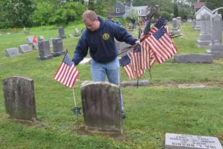 Ben Brick, a volunteer with Union Fire Company in Medford, places a flag on a veteran's grave in the township's Odd Fellows Cemetery. Since 2005,the men from the company have honored veterans and firefighters with the flags on the weekend before Memorial Day weekend.