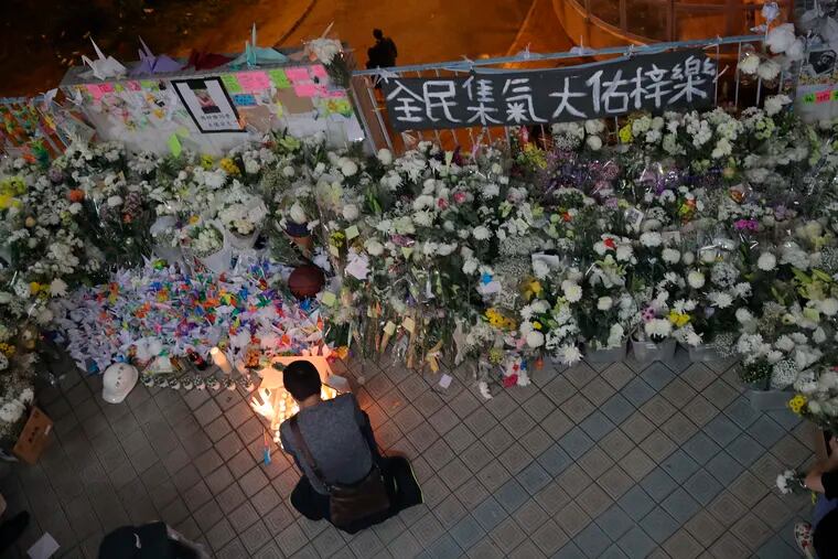 A protester light candles near flowers and a banner which reads "From all of us - God bless Chow Tsz-Lok" at the site where student Chow Tsz-Lok fell during a recent protest in Hong Kong on Friday, Nov. 8, 2019. Chow, a Hong Kong university student who fell off a parking garage after police fired tear gas during clashes with anti-government protesters died Friday in a rare fatality after five months of unrest, fueling more outrage against authorities in the semi-autonomous Chinese territory.