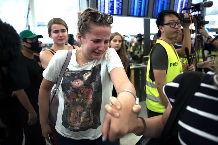Travelers react as they manage to walk through the protesters to the departure gates during a demonstration at the Hong Kong International Airport in Hong Kong, Tuesday, Aug. 13, 2019. Protesters severely crippled operations at Hong Kong's international airport for a second day Tuesday, forcing authorities to cancel all remaining flights out of the city after demonstrators took over the terminals as part of their push for democratic reforms.