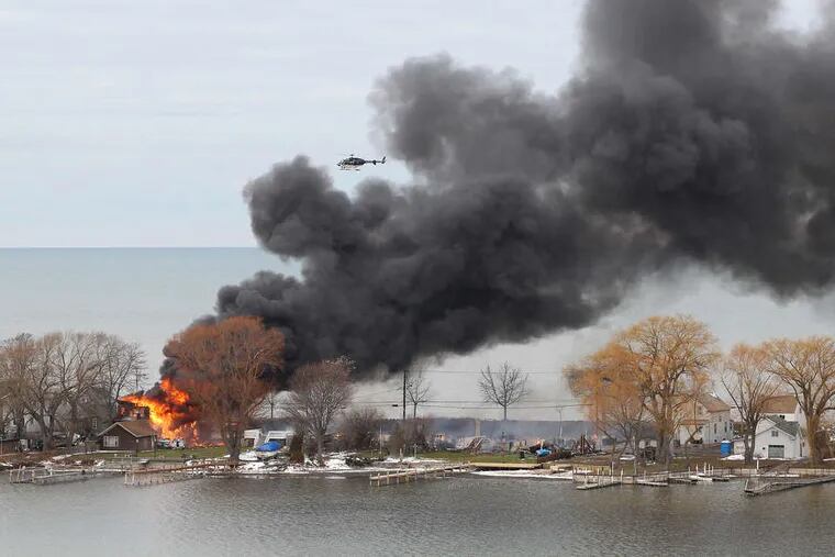 A helicopter passes over a burning house in Webster, N.Y., on Lake Ontario. A gunman held off firefighters and shot four.