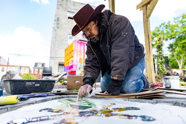 César Viveros, a multidisciplinary artist from Philadelphia, works on a center floor piece using stained glass in the outdoor kitchen at Iglesias Gardens.