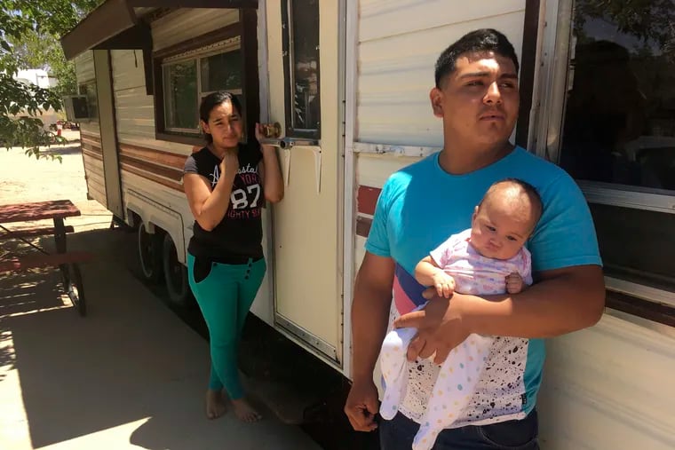 In this May 2018 photo, Jose Espinoza, 18, stands outside his trailer with his 4-month-old infant, Emmily, and wife, Maria Rodriguez, 19, in Vado, N.M., while speaking about making only $50 a day picking onions. New Mexico's child poverty rate rose slightly and continues to rank near the bottom nationally despite improvements in the state's economy, a child advocacy group said.