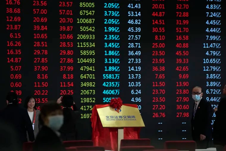 Attendees at an opening ceremony for the Beijing Stock Exchange passed near a display showing the stock market prices in Beijing, Monday, Nov. 15, 2021. A stock exchange set up in the Chinese capital to serve entrepreneurs opened trading Monday with 81 companies amid a crackdown on the country’s tech giants that has wiped more than $1 trillion off their market value abroad.