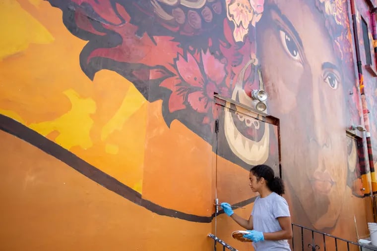 Natasha Perez, 29, the lead mural assistant and the face model for the mural, paints part of the mural at Providence Center in Fairhill, North Philadelphia.