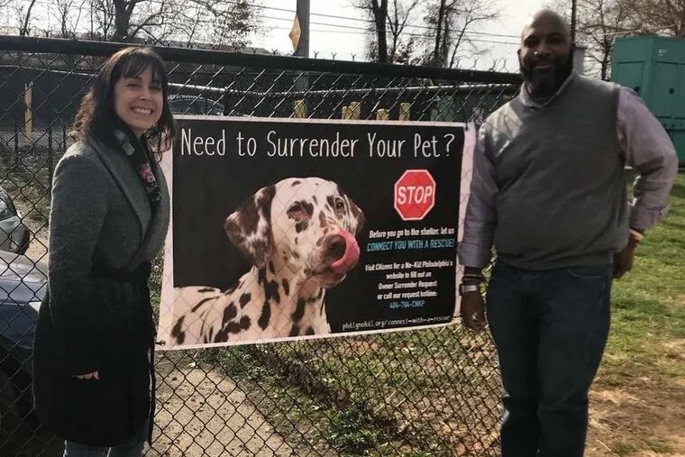 Samantha Holbrook, president of Citizens for a No-Kill Philadelphia (left) poses outside the ACCT Philly shelter in Feltonville with ACCT Philly executive director Vincent Medley, and a poster that urges pet owners to connect with a rescue group if they must surrender their pet.