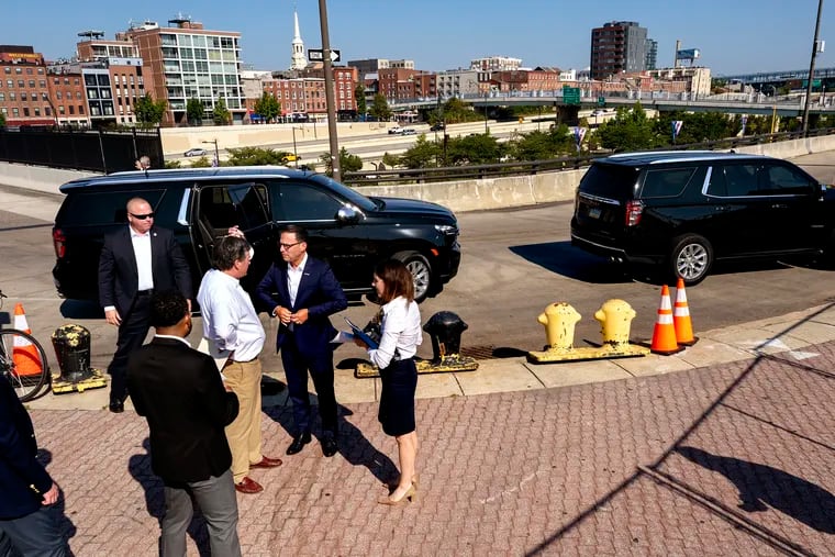 Pennsylvania Gov. Josh Shapiro (center) is greeted by PennDot Secretary Mike Carroll (left, no jacket) as he arrives for the official groundbreaking for the waterfront park over I-95 on the Great Plaza at Penn's Landing. Traffic on I-95 rolls past in the background. The Market Street Bridge at far right and the Chestnut Street Bridge is at left.