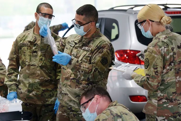 Members of the Illinois National Guard work with the public at the state's new drive-thru COVID-19 testing facility at Rolling Meadows High School Friday in Rolling Meadows, Ill. The test is self-administered by the person being tested, and the test kits are passed through the partially-opened car window.