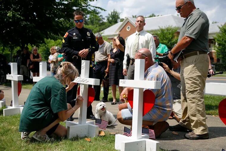A woman who did not wish to be identified writes a note on the back of a cross for Michelle Langer, a victim of a mass shooting at a municipal building in Virginia Beach, Va., at a nearby makeshift memorial, Sunday, June 2, 2019. (AP Photo/Patrick Semansky)