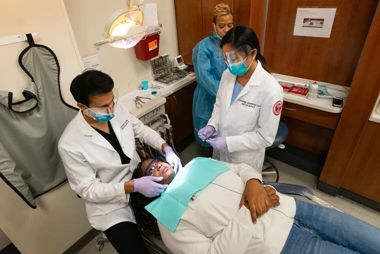 Dr. Adnan Kazim, Director of the Emergency Clinic, left, and Dr. Stephanie Serrano, 2nd year endodontic, front right, examine the teeth of Dennita Cunningham, center, a contract writer for the department of the treasury, at Temple University's dental school, in Philadelphia, Wednesday, January 23, 2019.