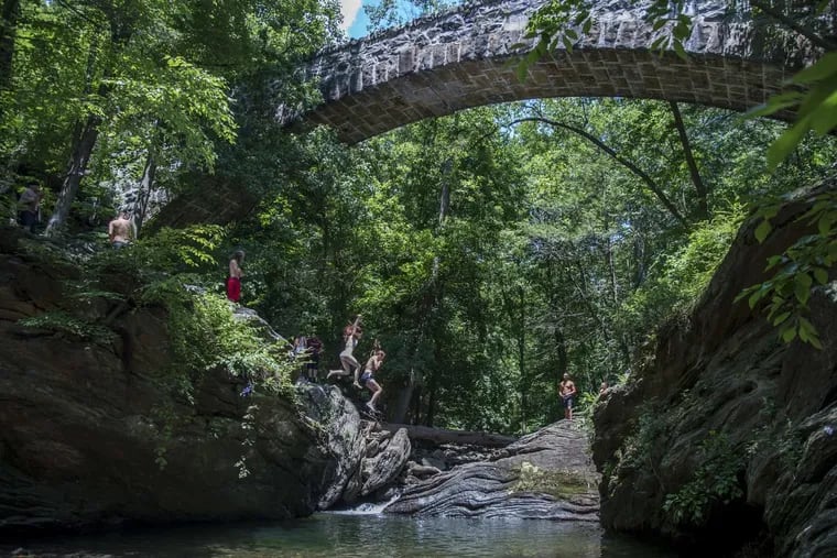 Two girls jump off the rocks at Devil's Pool in the middle of the Wissahickon creek on June 28, 2017.