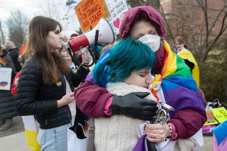Reese Grasso (center), a student at Central Bucks West High School, is hugged by Robi Gluck, a teacher in the Central Bucks School District, during a January rally to protest a school board vote that banned Pride flags and other "advocacy" materials from classrooms.