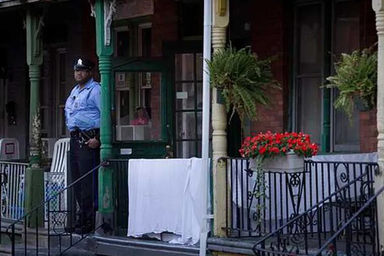 A Philadelphia police officer stands outside a home on the 2500 block of North Spangler Street in Strawberry Mansion, where a couple was found dead overnight (Alejandro Alvarez / Staff)
