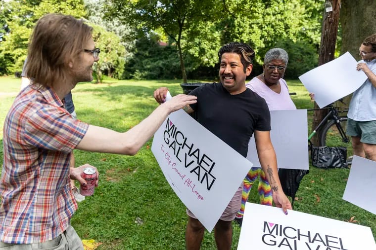 Michael R. Galvan, 32, hands Chris Anderko a sign on Saturday to show support for Galvan’s run for City Council at-large at Cloverly Park.