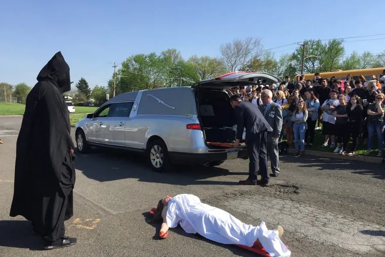 Truman High School students watch as classmate Marlee Jardine is loaded into the back of a hearse and Kyam Lewis hovers as the Grim Reaper during the annual mock car crash at the school.