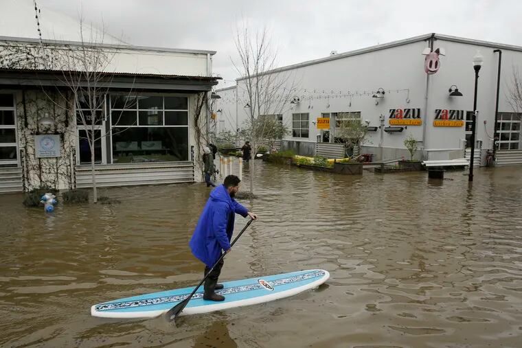 FILE - In this Wednesday, Feb. 27, 2019, file photo, a man uses a paddle board to make his way through the flooded Barlow Market District in Sebastopol, Calif. On Wednesday, March 6, 2019, the National Oceanic and Atmospheric Administration said that from December 2018 to February 2019 the Lower 48 states got 9.01 inches of rain and snow, which is 2.22 inches more than the 20th century normal.