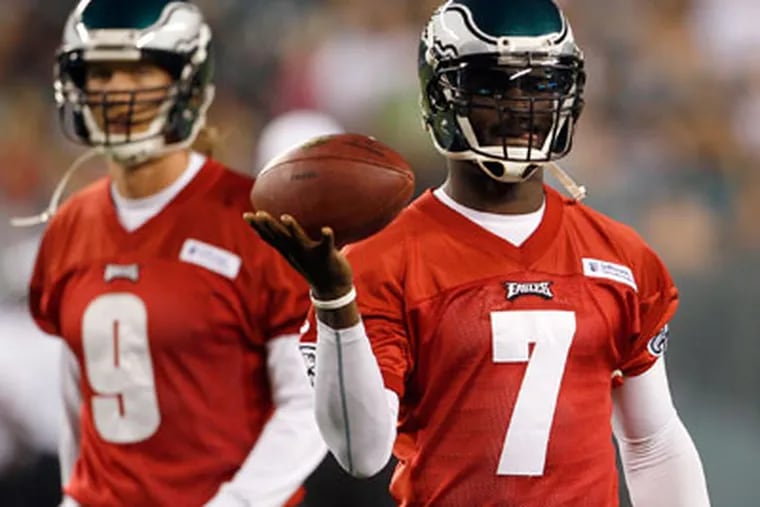 Eagles' quarterback Michael Vick holds the football as Nick Foles stands in the background during Flight Night full-team practice on Sunday, August 26, 2012.  ( Yong Kim / Staff Photographer )